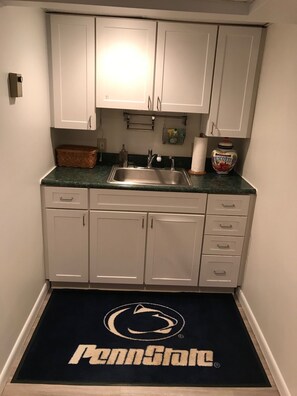 A kitchen with white cabinets, a stainless steel sink, and a Penn State logo doormat.