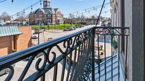 A balcony with a metal railing overlooking a street with cars and buildings, including a church with a steeple. - Downtown Urban Loft above Restaurants (Perryville)