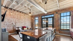 A spacious kitchen with a large island, exposed brick walls, and large windows providing natural light. - Downtown Urban Loft above Restaurants (Perryville)