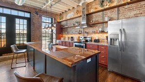A modern kitchen with a large island, stainless steel appliances, and a brick wall. - Downtown Urban Loft above Restaurants (Perryville)