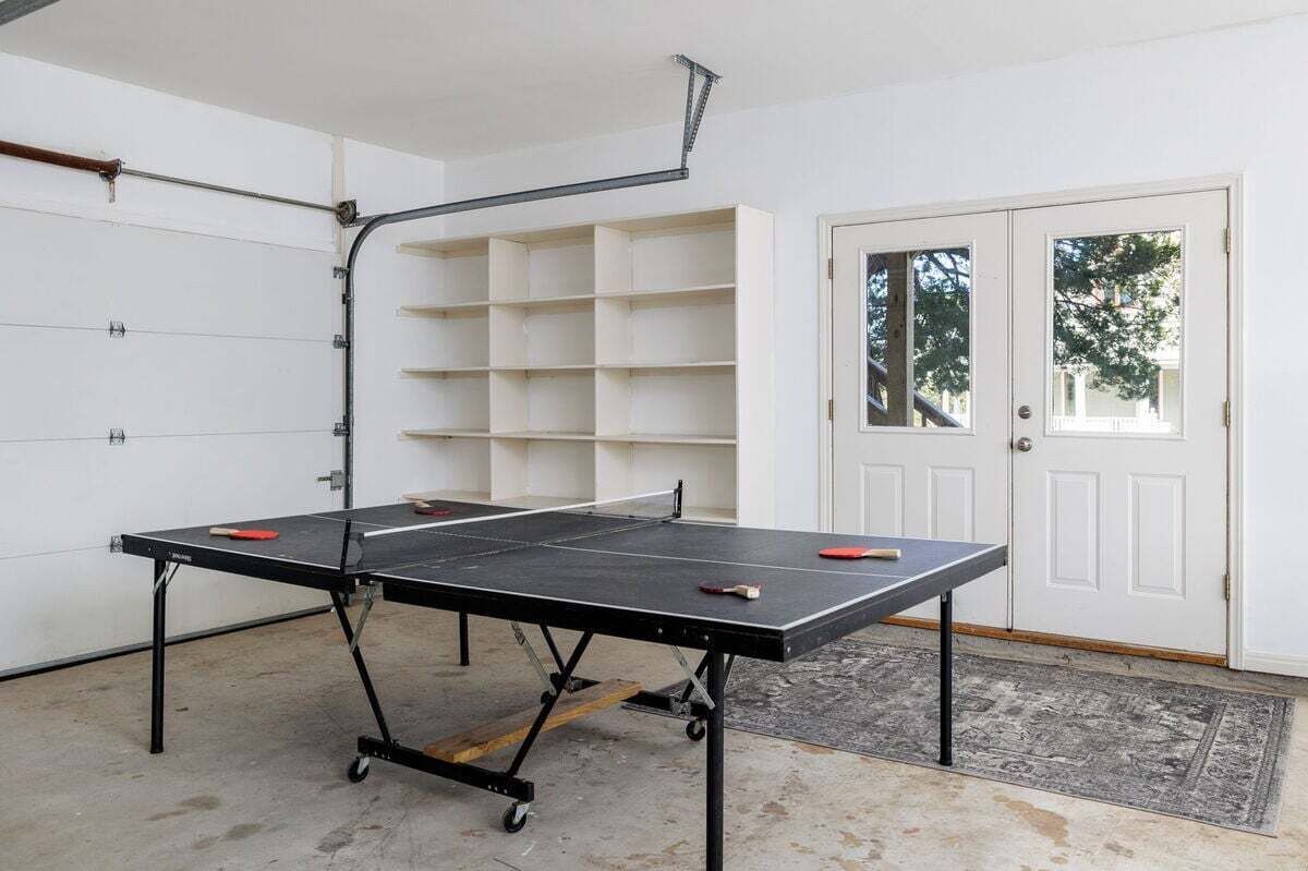 Une table de ping-pong dans une pièce avec une porte blanche et une porte de garage.