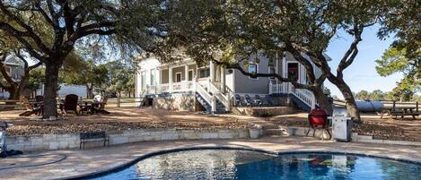A large house with a swimming pool, outdoor furniture, and a barbecue grill.
