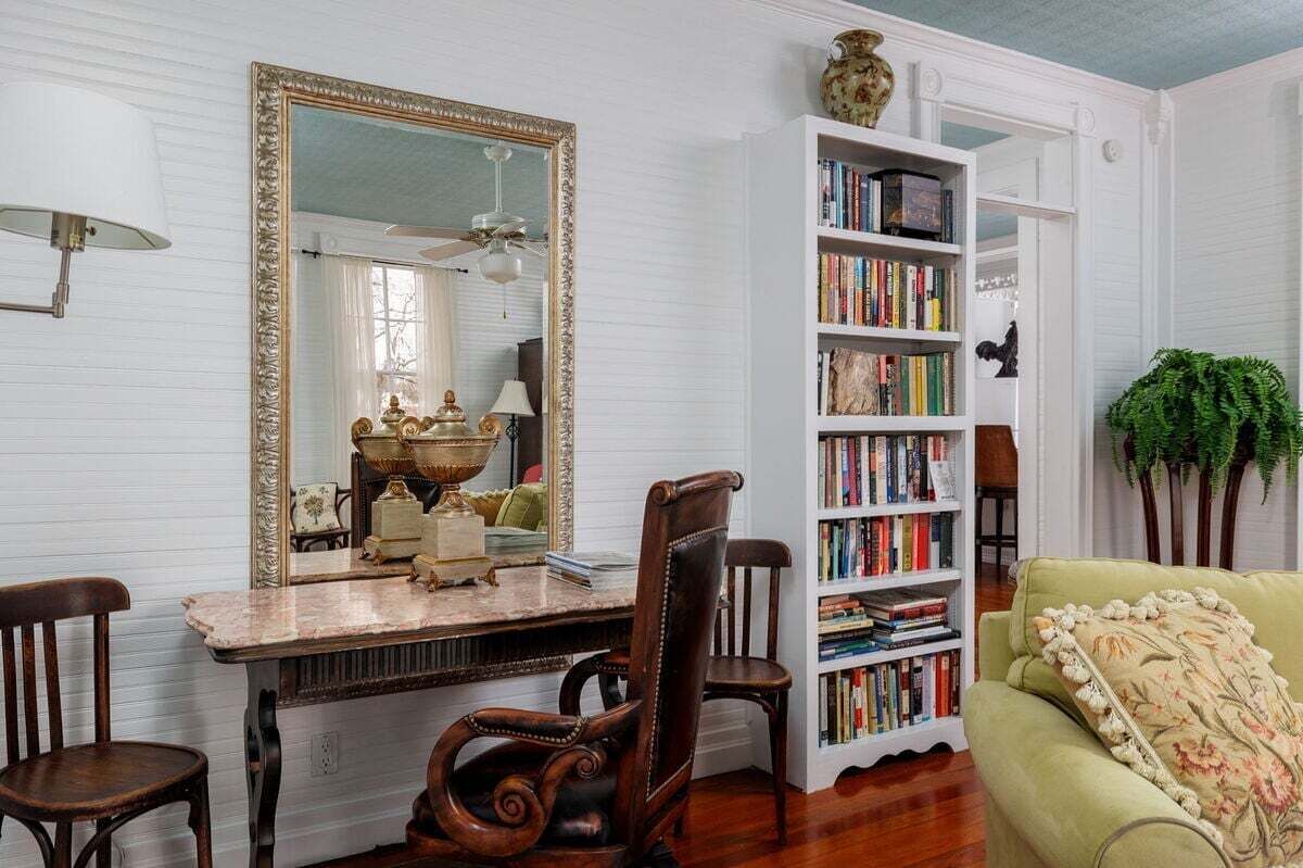 A room with a large mirror, a bookshelf, a dining table with chairs, and a green sofa.