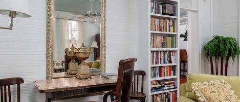 A room with a large mirror, a bookshelf, a dining table with chairs, and a green sofa.