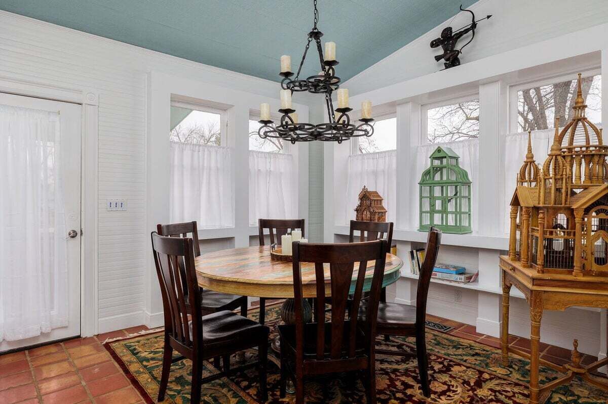A dining room with a round table, chairs, a chandelier, and decorative birdcages.