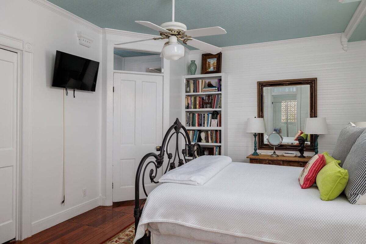Une chambre à coucher comprenant un lit, un ventilateur de plafond, une bibliothèque, un téléviseur et un miroir.