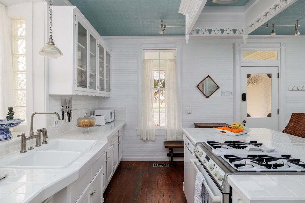 A kitchen with white cabinetry, a stove, a sink, and a window with a view.