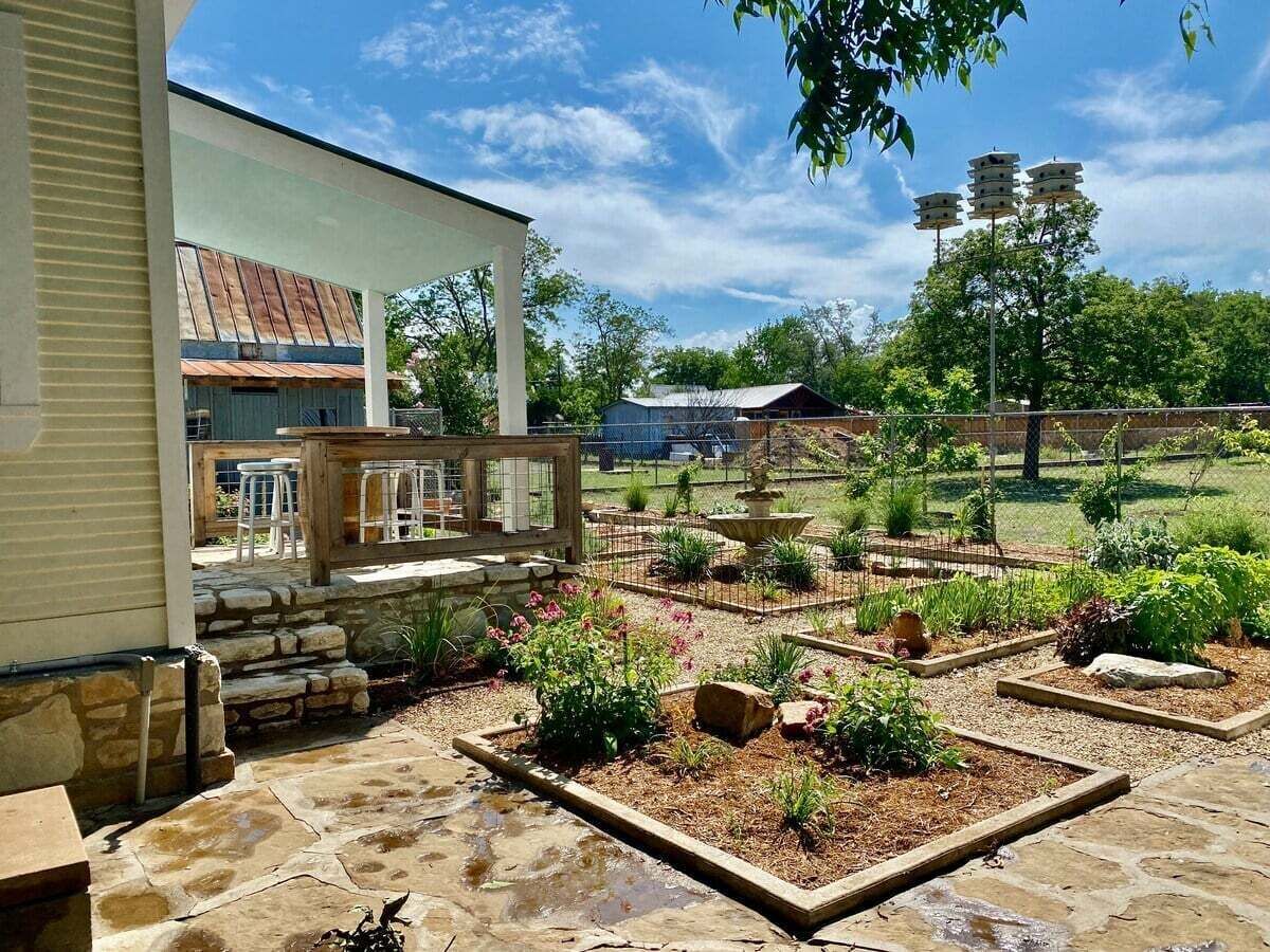 Een terras met stenen vloer, een houten terras en een tuin met verhoogde planters en een fontein.