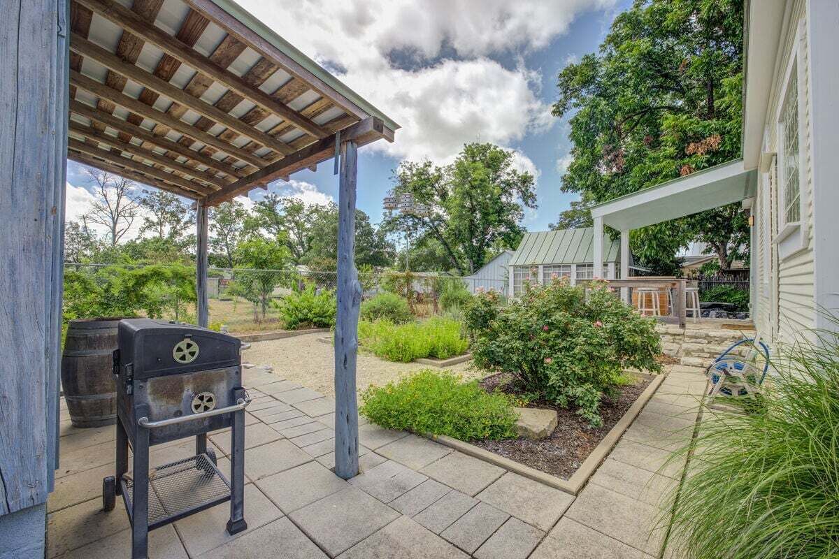 A covered patio with a grill, a garden with various plants, and a house in the background.
