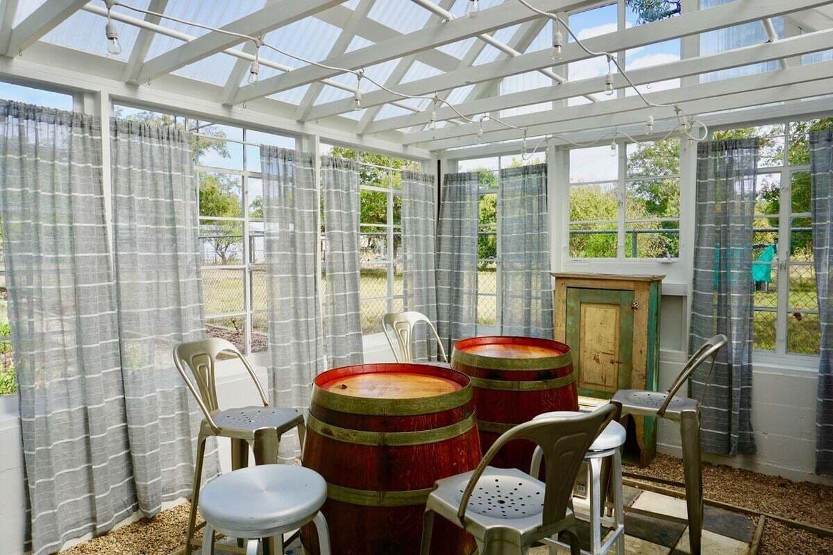 A conservatory with a glass ceiling, wooden barrels, and plastic chairs.