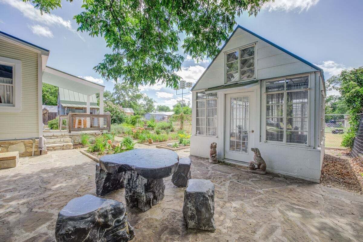 Ein Haus mit einer Steinterrasse, einem überdachten Außenbereich und einem kleinen Garten.