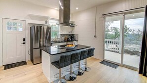 Uma cozinha moderna com ilha central, eletrodomésticos de aço inoxidável e porta de vidro deslizante para uma varanda.