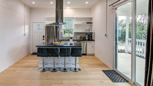 Cozinha moderna com ilha central, banquetas, exaustor de aço inoxidável e porta de vidro deslizante para uma varanda.