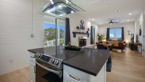 Cozinha moderna com ilha central, área de jantar com sofá e mesa, e lareira.