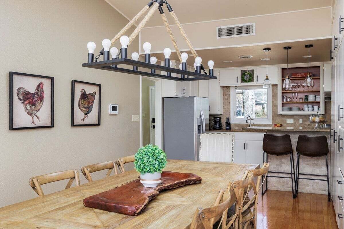 Un comedor con una mesa de madera, sillas, una planta en maceta y una lámpara colgante.