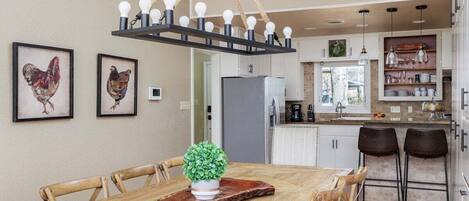 Un comedor con una mesa de madera, sillas, una planta en maceta y una lámpara colgante.