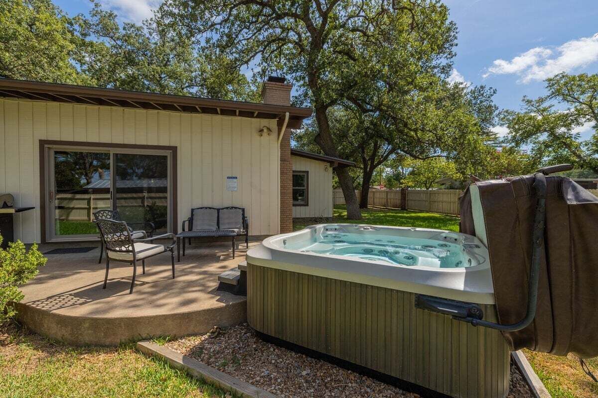 A backyard with a hot tub, patio furniture, and a house with a sliding glass door.