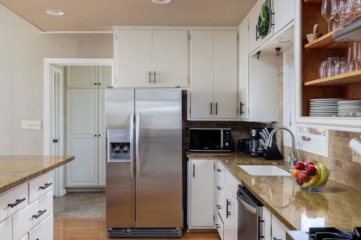 A kitchen with white cabinets, a stainless steel refrigerator, a microwave, and a fruit bowl on the counter.