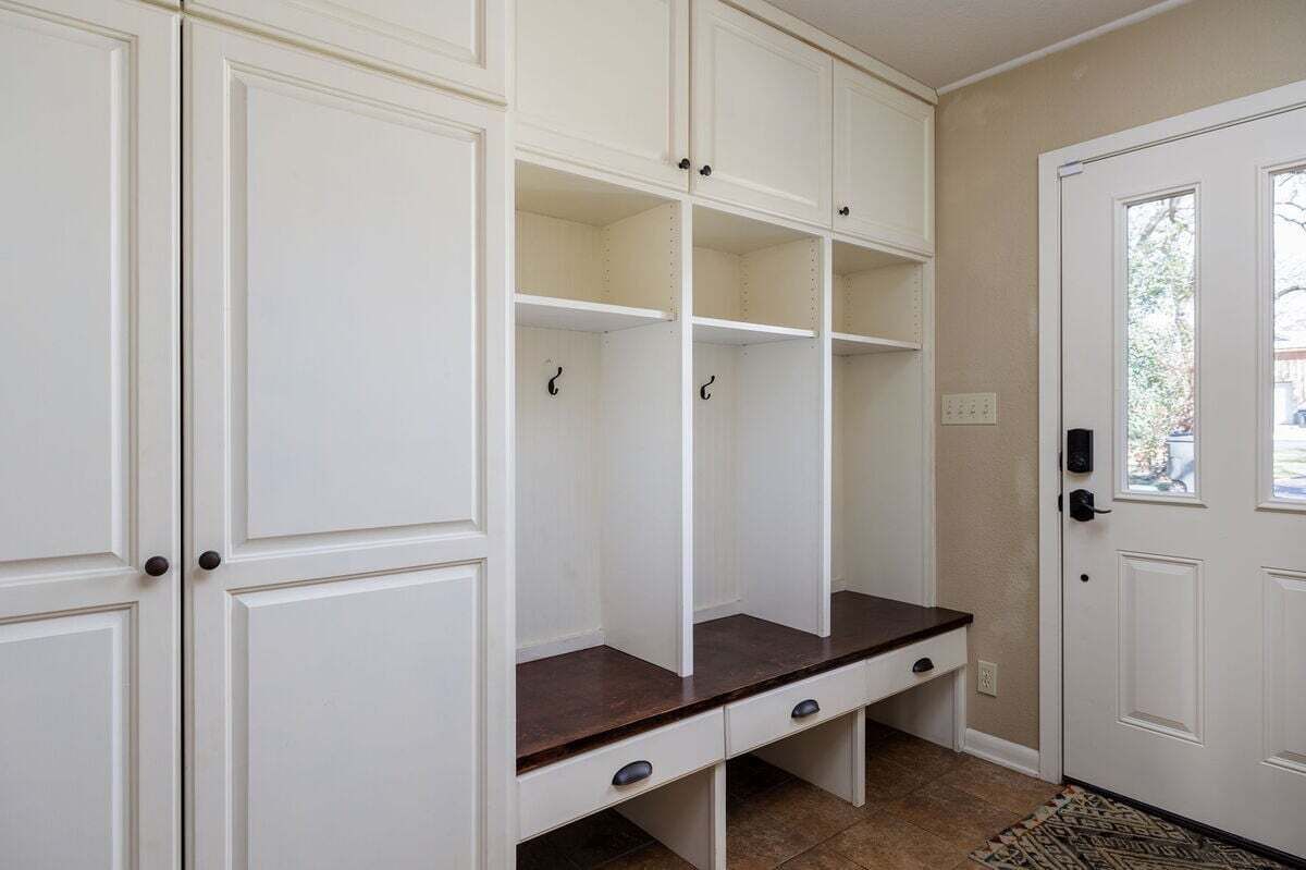 Una habitación con muebles blancos, un banco de madera oscura y una puerta con ventana.