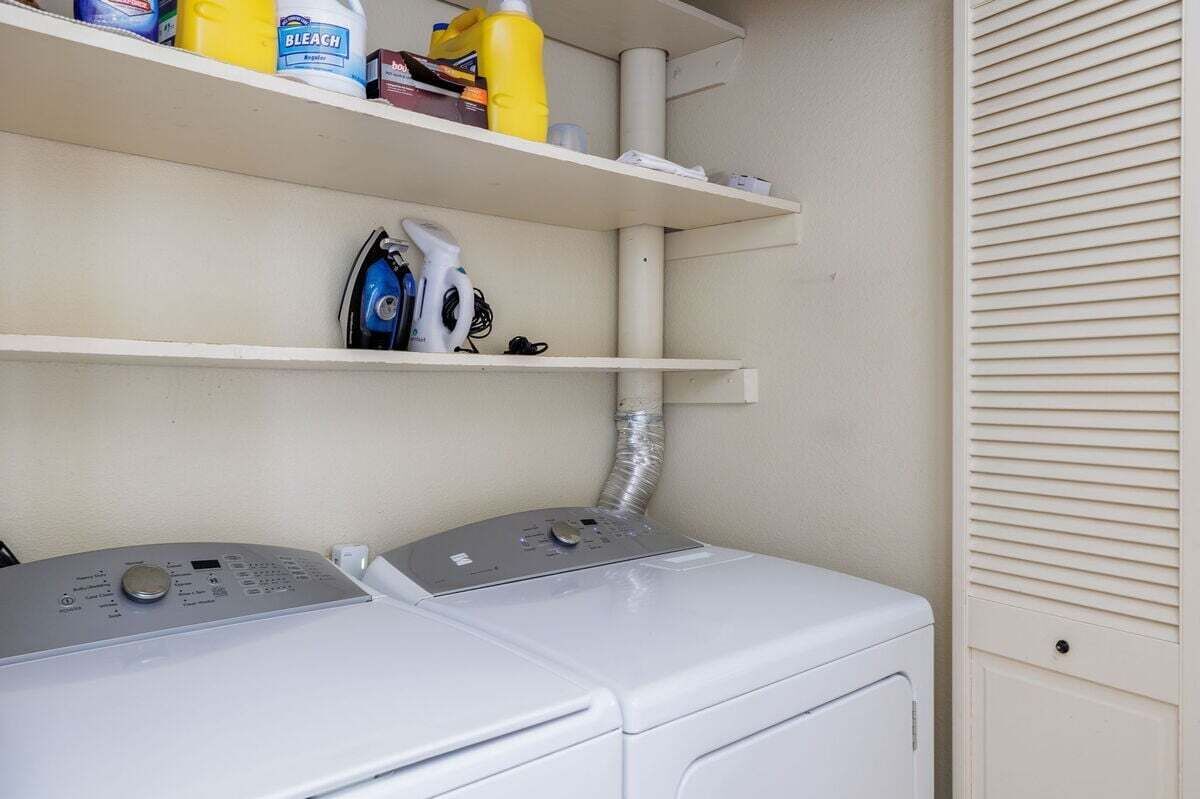 Een wasruimte met twee wasmachines, een plank met schoonmaakmiddelen en een ventilatiepijp.