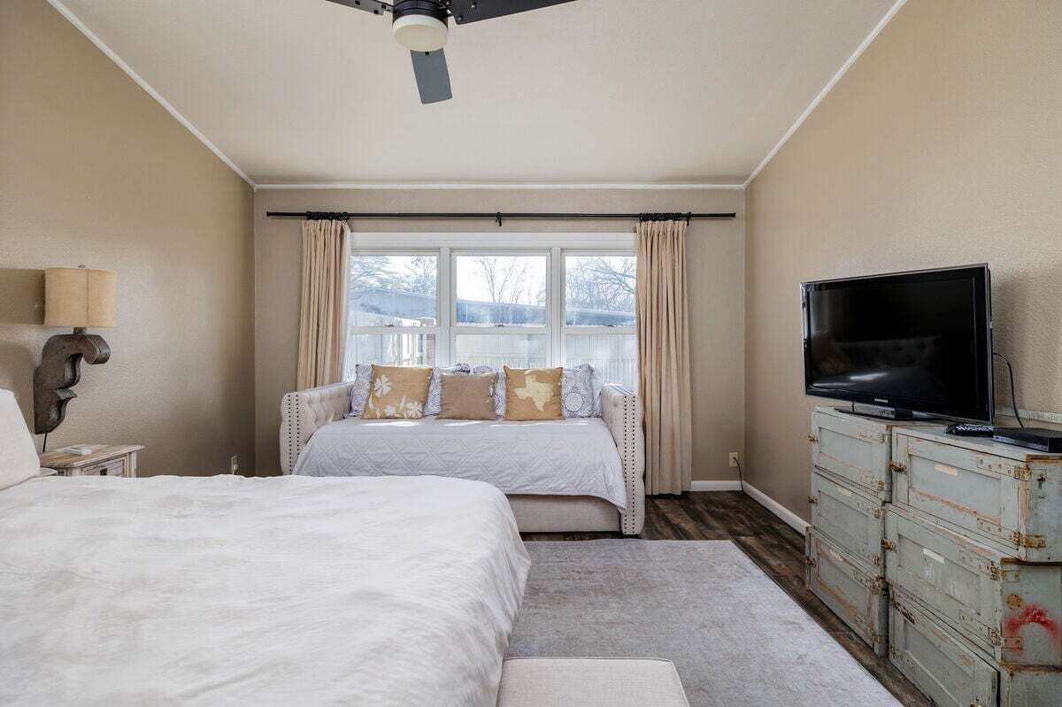 A bedroom with a bed, a TV, a dresser, and a window with curtains.