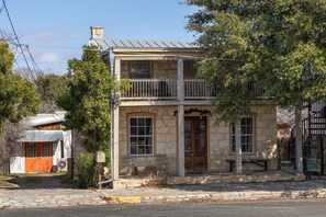 A two-story stone building with a balcony, a wooden door, and a mailbox. - Historic Rumpel Kammer - Steps to Main (Fredericksburg)