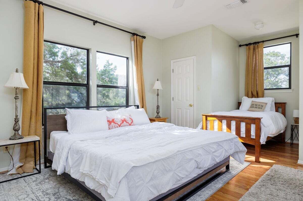 Un dormitorio con dos camas, ventanas amplias, una puerta y una mesita de noche con lámpara.