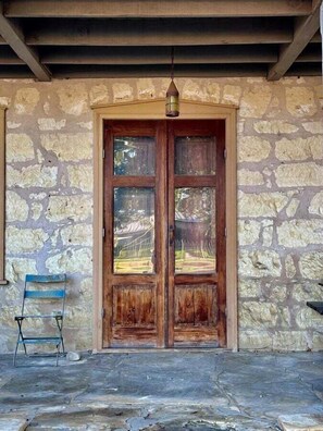 A stone building with a wooden door, a hanging light fixture, and a blue chair outside. - Historic Rumpel Kammer Compound (Fredericksburg)