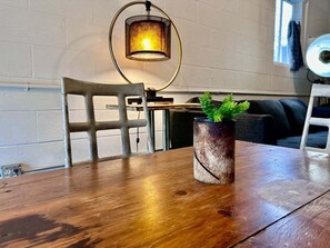 A wooden table with a potted plant, a chair, a wall-mounted lamp, and a couch in a room with white brick walls. - Historic Rumpel Kammer Compound (Fredericksburg)