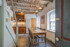 A dining area with a wooden table and chairs, a kitchen with wooden cabinets, and a rustic ceiling. - Historic Rumpel Kammer Compound (Fredericksburg)