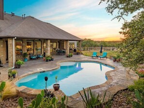 A swimming pool with a stone border, surrounded by potted plants and outdoor furniture. - Hill Country Escape-670 Heather Hills (Dripping Springs)