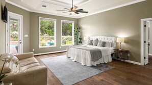 A bedroom with a bed, a ceiling fan, a TV, and large windows. - Hill Country Escape-670 Heather Hills (Dripping Springs)