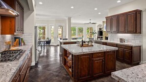 A spacious kitchen with dark wood cabinets, granite countertops, and a central island. - Hill Country Escape-670 Heather Hills (Dripping Springs)