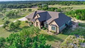 A large house with a stone exterior, multiple roofs, and a spacious yard. - Hill Country Escape-670 Heather Hills (Dripping Springs)