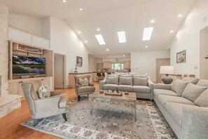 A spacious living room with a large flat-screen TV, a sofa set, a coffee table, and a patterned rug. - Pool, Tennis & Pickleball Ultimate Hill Country Retreat Creek Sleeps 10 (Dripping Springs)