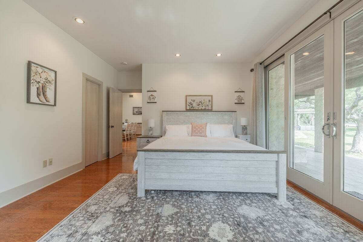 A bedroom with a large bed, a patterned rug, and a sliding glass door leading to an outdoor area.