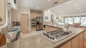 Une cuisine moderne dotée d’appareils électroménagers en acier inoxydable, d’un grand îlot central avec une cuisinière à gaz et offrant une vue sur l’extérieur.