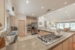 A modern kitchen with stainless steel appliances, a large island with a gas stove, and a view of the outdoors. - Pool, Tennis & Pickleball Ultimate Hill Country Retreat Creek Sleeps 10 (Dripping Springs)