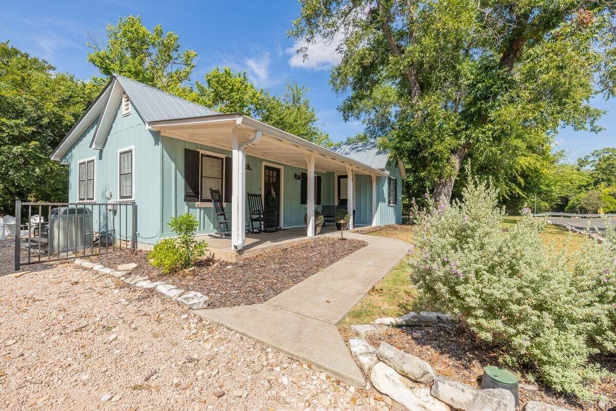A light blue house with a covered porch, a gravel driveway, and a small garden area.