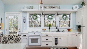 Una cucina con mobili bianchi, un fornello, un lavandino e una finestra con una ghirlanda.