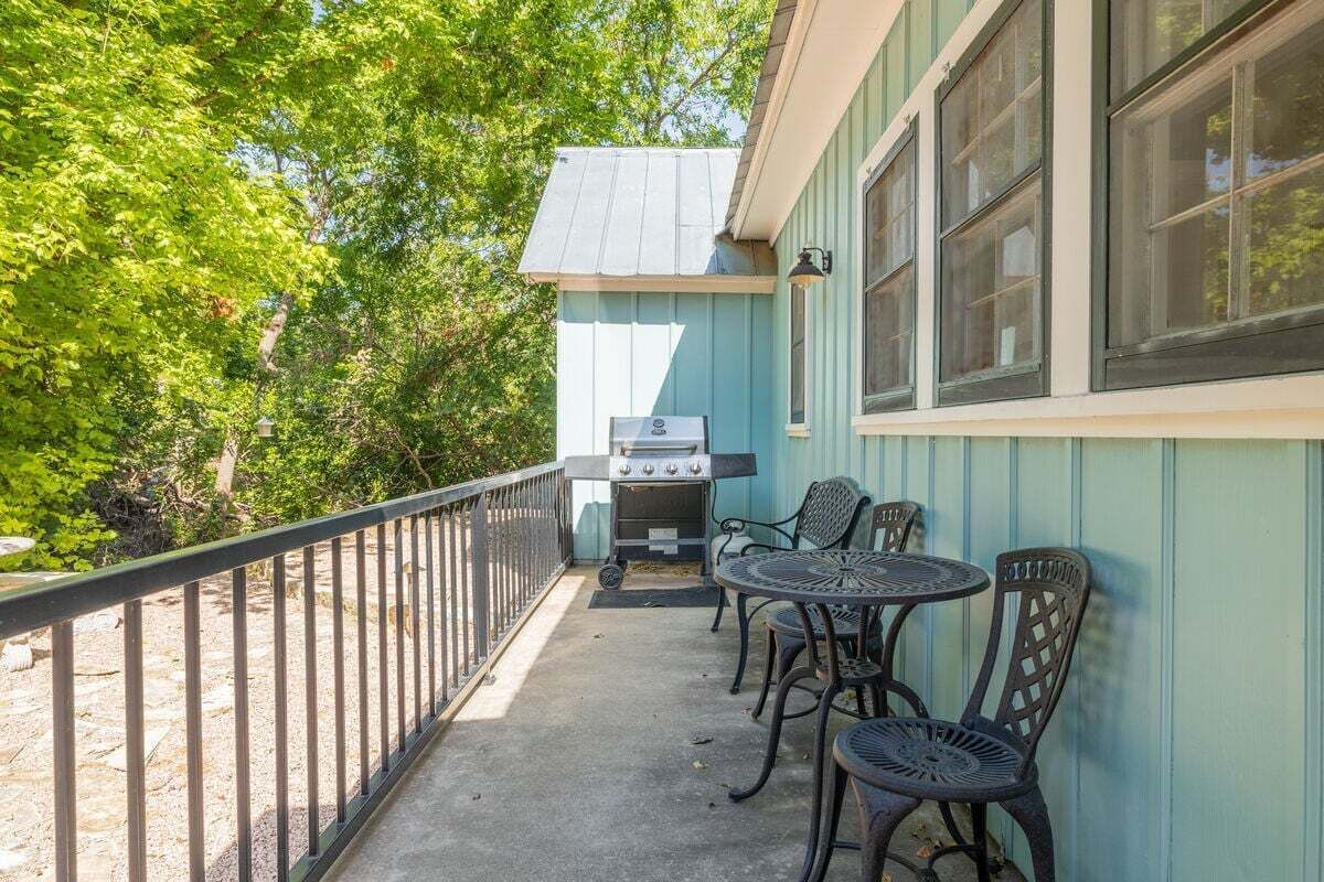 En overdækket terrasse med grill, udendørs møbler og udsigt til en bygning med store vinduer.