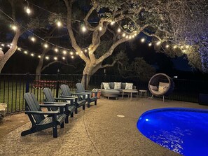 Un área de piscina al aire libre con luces colgantes, sillas tipo Adirondack y un espacio de estar circular.