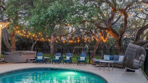 Uma piscina com cadeiras e um sofá, cercada por árvores e luzes de corda.