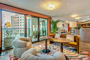 Ein modernes Hotelzimmer mit großem Fenster, einer Couch, einem runden Tisch und einer Zimmerpflanze.