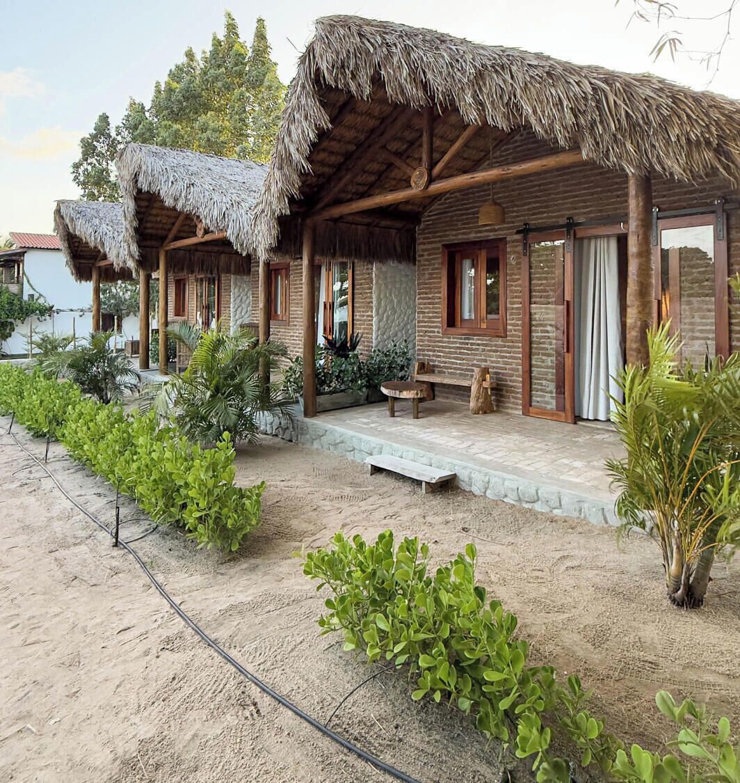 A rustic building with thatched roofs, a stone pathway, and lush greenery.