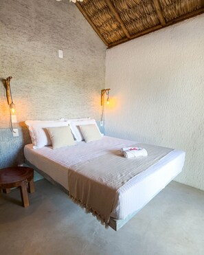 A single bed with a white bedspread, two wall-mounted lights, a small wooden stool, and a textured ceiling.