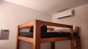 Ein Etagenbett mit Holzrahmen, eine Wandklimaanlage und ein kleines gerahmtes Bild an der Wand.