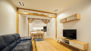 Una sala de estar moderna con sofá de cuero, mesa de centro de madera, mueble para televisión y cocina al fondo.