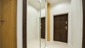 Un pasillo con una puerta de madera, un espejo y otra puerta de madera al final.