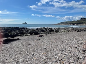 Una playa rocosa con una isla distante, cielo despejado y mar tranquilo.